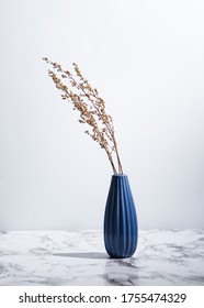 Minimalist photo of blue vase with dried plants on marble surface on light background