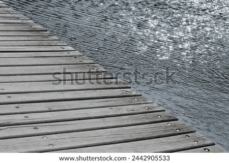 Minimalist photo of water and wooden pier diagonally divided into two halves. The surface of the water is calm, shimmering in the sun. Muted colors. 