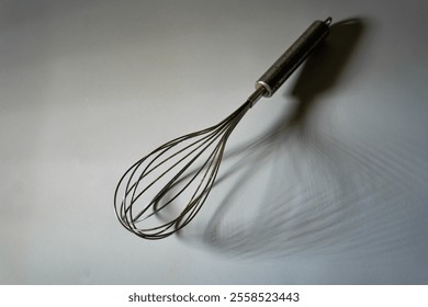 Minimalist photograph of a stainless steel whisk with artistic shadow on a plain background. Ideal for culinary themes - Powered by Shutterstock