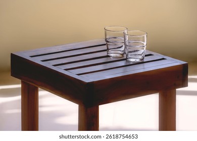 Minimalist phtograph with 2 partially filled water glasses on a wooden table top.