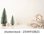 Minimalist Scandinavian Christmas side view scene featuring miniature snow-covered trees and a wooden house on a cozy knit blanket