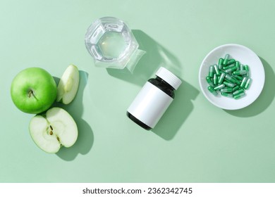 Minimalist scene for advertising product with ingredient from green apple. An unlabeled bottle with green apple slices and dishes of capsule pills decorated on green background - Powered by Shutterstock