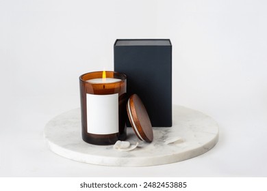 minimalist scented candle packaging or branding mockup with with burning candle in an amber glass jar with label, wooden lid, black cardboard box and white flower petals on a round white marble plate
 - Powered by Shutterstock