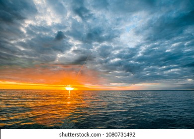 Minimalist Seascape - Stormy Clouds Over Calm Waters With Sun Touching The Horizon