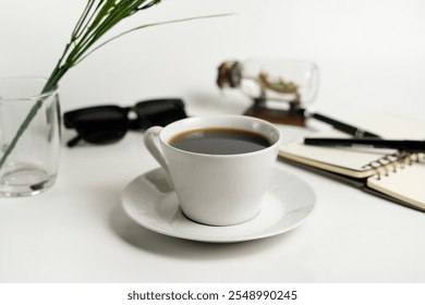 A minimalist setup featuring a cup of black coffee, sunglasses, notebook, and pen on a white background. Ideal for concepts of relaxation, planning, and creativity. - Powered by Shutterstock