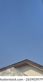 A minimalist shot featuring the sharp angle of a building's brown roofline against a vast, clear blue sky. The clean lines of the architecture contrast with the expansive open space