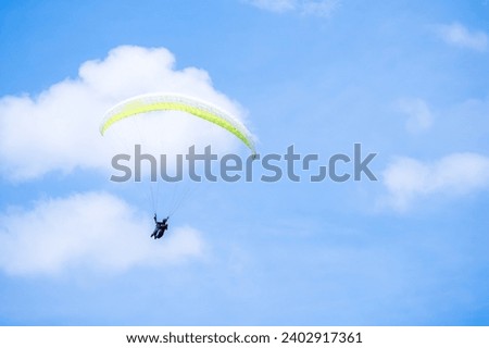 Minimalist shot of a man with a para-gliding over bright blue sky and fluffy white cloud