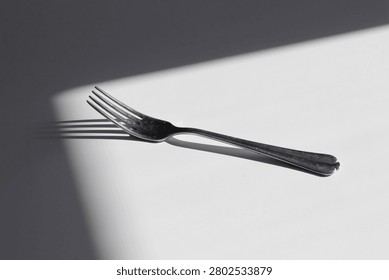 Minimalist silver fork with soft shadow isolated on white background. Modern aesthetic kitchen concept. Cuttlery placed on white table in corner of shadows.