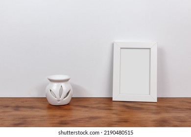 Minimalist Still Life Of A Customizable Picture Frame And White Essence Burner. Wood And White Background