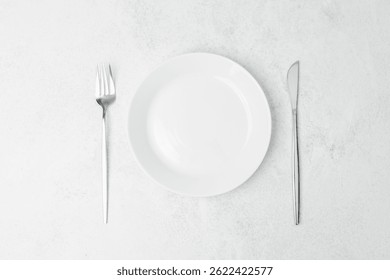 A minimalist table setting featuring an empty white plate, fork, and knife.