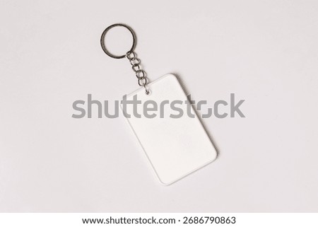 Minimalist top view of a blank rectangular white keychain with a metal ring and chain placed on a clean white background, ideal for mockups or branding presentations.