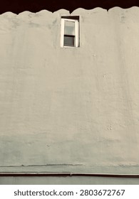 A minimalist view of a lone rectangular window centered on a textured, weathered beige wall, captured in a monochromatic tone.