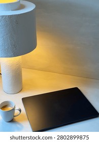A minimalist workspace setup featuring a lamp, coffee mug, laptop, and wooden desk surface.