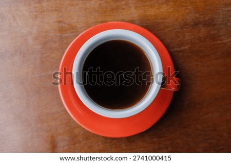 A minimalist yet authentic top-down view of black coffee in a vibrant red cup on an earthy, textured wooden table. This image embraces a handcrafted aesthetic over synthetic perfection, utilizing natural cafe lighting.