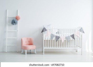 Minimalistic baby's room interior with an elegant, small, chic, pink chair, a decorated ladder, and a child's bed