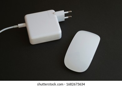 Minimalistic combination of white mouse and charger for laptop on the dark background.