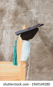 Minimalistic Composition Of 2021 Graduation. Graduation Hat And Medical Mask On The Chair. Photo Is Soft Colors