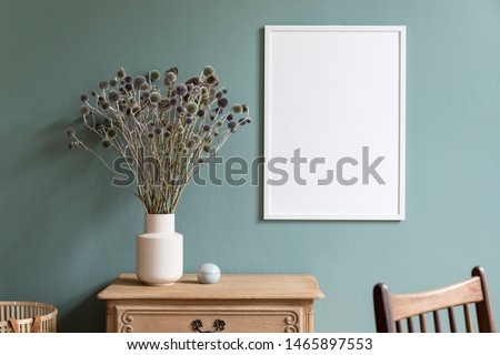 Minimalistic composition of sitting room interior with white mock up frame, wooden shelf, retro chair, rattan basket and elegant accessories. Design home decor. Template. Eucalyptus color concept.