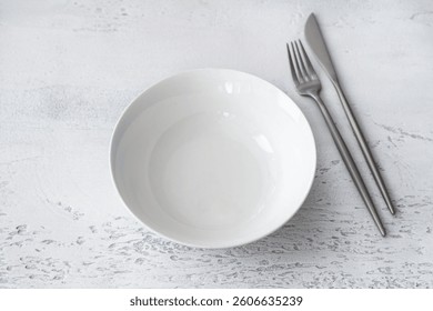Minimalistic dining setup with white ceramic bowl and stainless steel Ccutlery on grey surface
