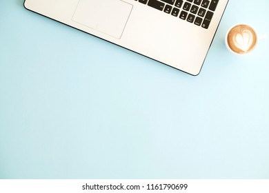 Minimalistic flat lay composition of black & white laptop computer keyboard & cup of cappuccino coffee on baby blue surface desk table background in bright light. Workspace top view, copy space