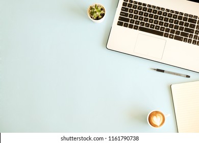 Minimalistic flat lay composition of black & white laptop computer keyboard, cell phone, coffee cup, blank page notebook on baby blue surface desk table background. Workspace top view, copy space.