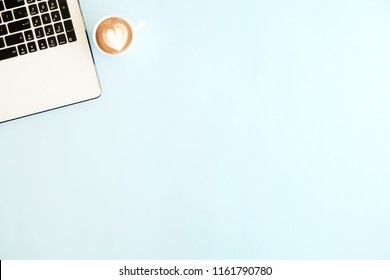 Minimalistic flat lay composition of black & white laptop computer keyboard & cup of cappuccino coffee on baby blue surface desk table background in bright light. Workspace top view, copy space