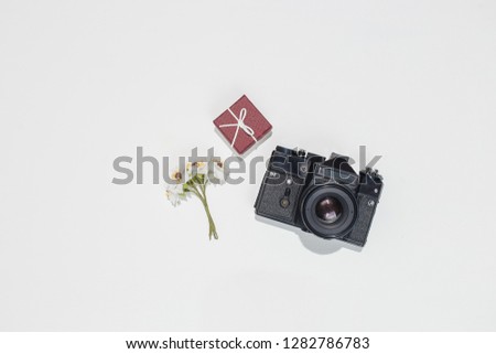 Minimalistic flat lay composition with retro camera, vinous gift box and spring field flower on white background. Trendy flat lay mockup for bloggers, designers, photographers, etc.