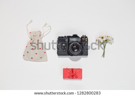 Minimalistic flat lay composition with retro camera, red gift box, canvas bag with red heart shapes and spring field flower on white background. Trendy flat lay mockup for bloggers, designers