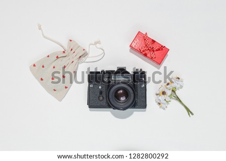 Minimalistic flat lay composition with retro camera, red gift box, canvas bag with red heart shapes and spring field flower on white background. Trendy flat lay mockup for bloggers, designers