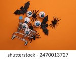 Minimalistic Halloween layout with eyeballs, bats and spiders in shopping cart on orange background