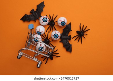 Minimalistic Halloween layout with eyeballs, bats and spiders in shopping cart on orange background - Powered by Shutterstock