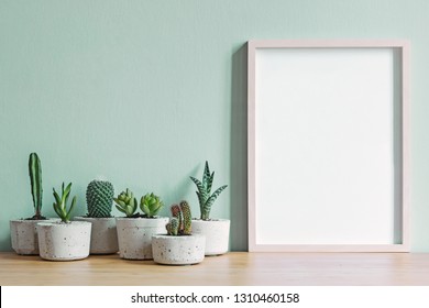 Minimalistic Home Interior With Mock Up Photo Frame On The Brown Wooden Table With Composition Of Cacti And Succulents In Stylish Cement Pots. Mint Walls. Stylish Concept Of Home Garden.