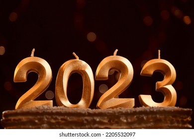 Minimalistic Horizontal Burgundy Background With Bright Yellow Bokeh Garland And Copy Space. Holiday Background Happy New Year. Candles Without Fire Stuck In Cake. Numbers 2023 Made By Gold Candles.