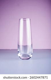 minimalistic image featuring an elegant, transparent glass half-filled with water, set against a pastel purple backdrop that transitions subtly into a serene, cool blue surface. plain, contrast