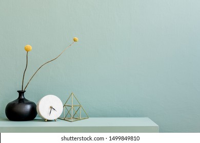 Minimalistic interior design of living room at nice apartment with stylish shelf, vase with flowers, gold pyramid, clock and elegant accessories. Copy space. Eucalyptus color concept. Template.