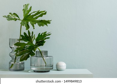 Minimalistic interior design of living room at nice apartment with stylish shelf, glassy vases with tropical flowers and elegant accessories. Copy space. Eucalyptus color concept. Template. 