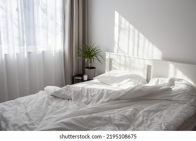 Minimalistic modern bedroom with white bedding and grey curtains. Morning light from the window falling on a bed with white satin bedding.  - Powered by Shutterstock