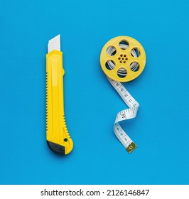 Minimalistic photo of a yellow stationery knife and a stylish measuring tape on a blue background. Tools for creativity. Flat lay.