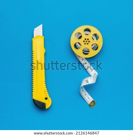 Minimalistic photo of a yellow stationery knife and a stylish measuring tape on a blue background. Tools for creativity. Flat lay.