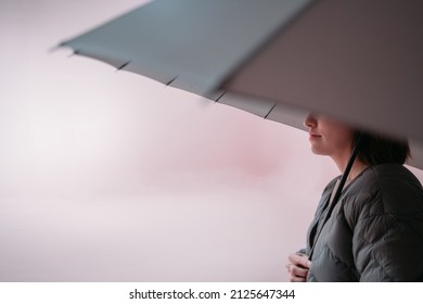 Minimalistic portrait of a girl with an umbrella on a uniform background. The concept of security and protection. Young woman in a light jacket with a large umbrella over her head in a room  - Powered by Shutterstock