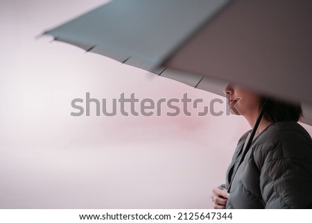Minimalistic portrait of a girl with an umbrella on a uniform background. The concept of security and protection. Young woman in a light jacket with a large umbrella over her head in a room 