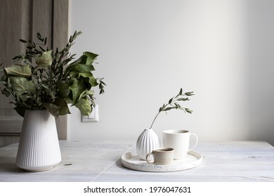 Minimalistic Scandinavian style. Half-open branches of an apple tree in a white fluted vase. A small vase with a branch of dried eucalyptus and two cups of coffee on a tray on the table.