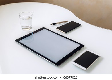 A Minimalistic Set Of Black And White Business Accessories And Digital Devices Laying On A Crystally White Table With Curvy Shape: A Phone, A Tablet, A Notebook, A Glass Of Water, Side View