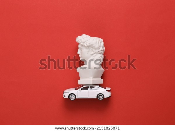 Minimalistic still life. Bust of David on a\
model car, red\
background