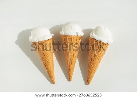 Minimalistic summer composition featuring three waffle ice cream cones with scoops of vanilla ice cream on a clean white table.