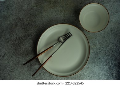 Minimalistic Table Setting  With White Ceramic Dinnerware And Cutlery On Concrete Table