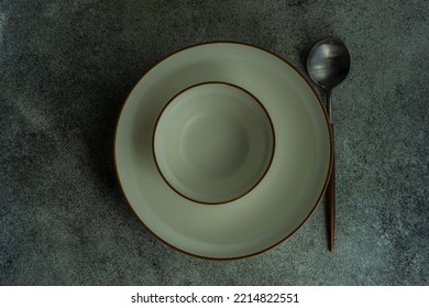 Minimalistic Table Setting  With White Ceramic Dinnerware And Cutlery On Concrete Table