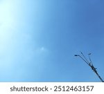 Minimalistic view of a streetlight against a clear blue sky with a small cloud