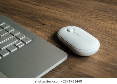 A minimalistic workspace featuring a white wireless computer mouse and a laptop on a wooden desk. Perfect for technology, remote work, or business concepts with a clean and simple look.