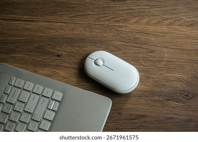 A minimalistic workspace featuring a white wireless computer mouse and a laptop on a wooden desk. Perfect for technology, remote work, or business concepts with a clean and simple look.